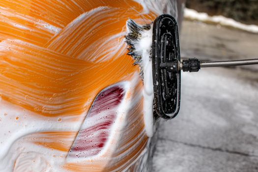 Detail on brush leaving strokes in soap and foam of a yellow car washed.