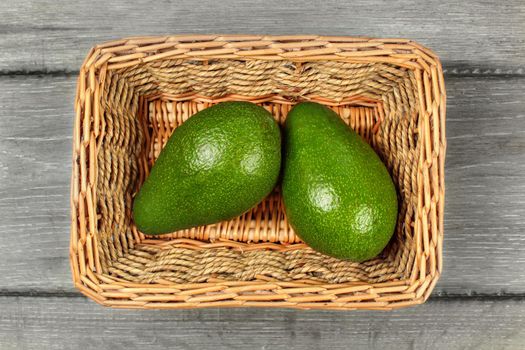 Table top view - two whole avocado pears in rectangular basket.