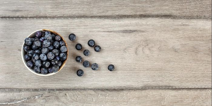 Table top view - small bowl with blueberries, some of them spilled on gray wood desk. Banner with space for text on the right.