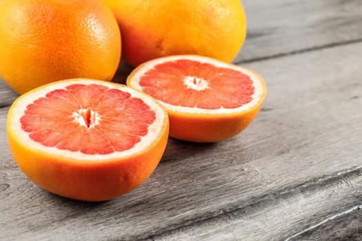 Pink red grapefruit cut in half, with two whole in background on gray wood table.