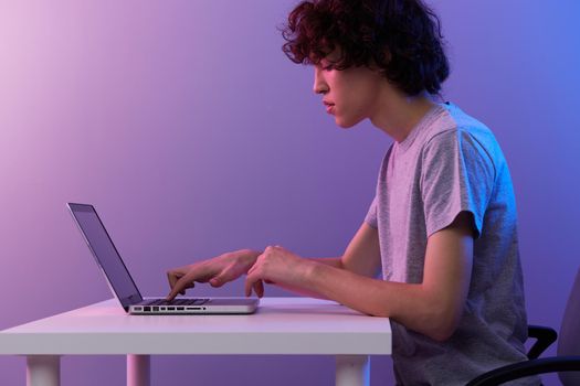 gamer sitting at the table gaming laptop violet background. High quality photo