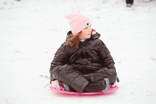 Active girl sliding down the hill. Happy child having fun outdoors in winter on sledge. Family time