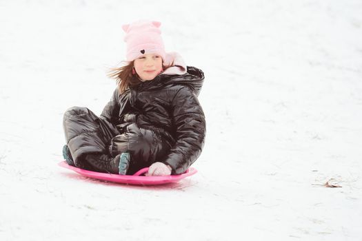 Happy little girl sliding down the hill on saucer sled. Girl enjoying slider ride on the snow.