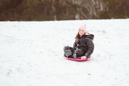 Active girl sliding down the hill. Happy child having fun outdoors in winter on sledge. Family time