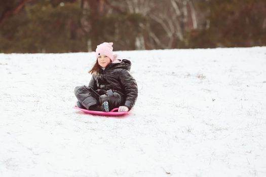 Happy little girl sliding down the hill on saucer sled. Girl enjoying slider ride on the snow.