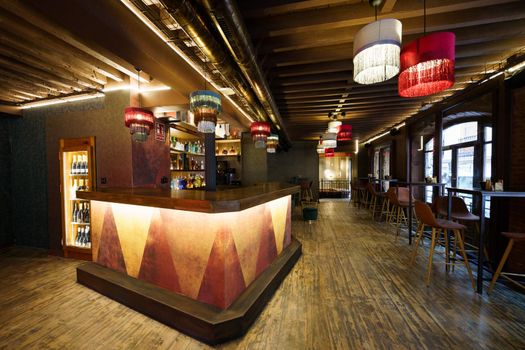 Modern interior of cafe with wooden counter and comfortable chairs at tables under glowing chandeliers