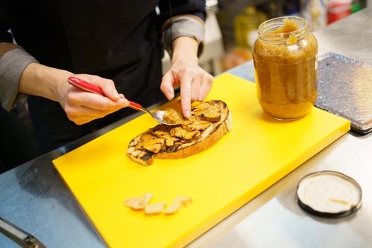From above, anonymous chef putting pieces of foie on a piece of fried bread, while cooking bruschetta in a restaurant kitchen.