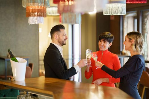 Company of cheerful friendly people in elegant outfits clicking glasses with champagne and proposing toast while celebrating event in restaurant