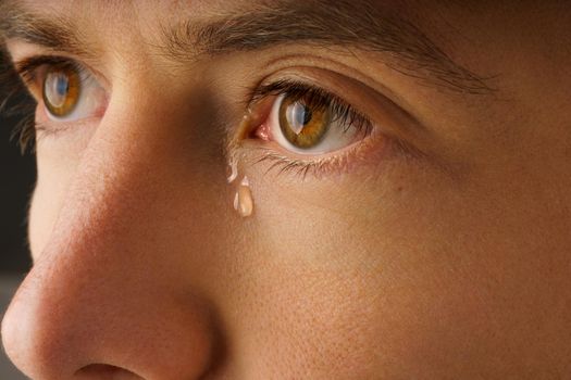 Closeup photo of young man eye with a tear. Man crying. High quality photo