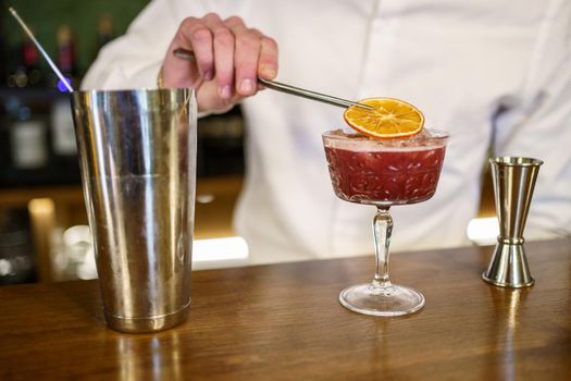 Unrecognizable male barkeeper putting dried slice of orange on top of cold fruit cocktail placed on counter in pub