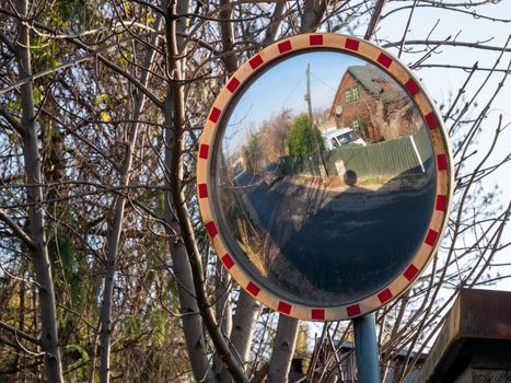 Corner road round mirror with trees on background. Mirror to help transport.
