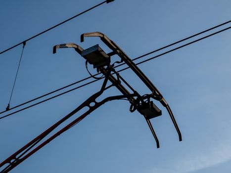 Pantograph of a train connecting on electric line on blue daylight sky background