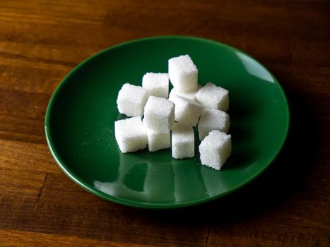 Sugar cubes on a green plate and on a wooden table