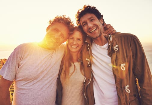 Portrait of three friends standing on a hill top at sunset