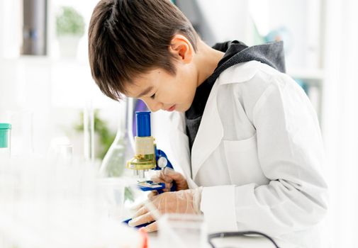 School boy doing chemistry experiment in elementary science class with microscope. Clever pupil with tubes in lab during test