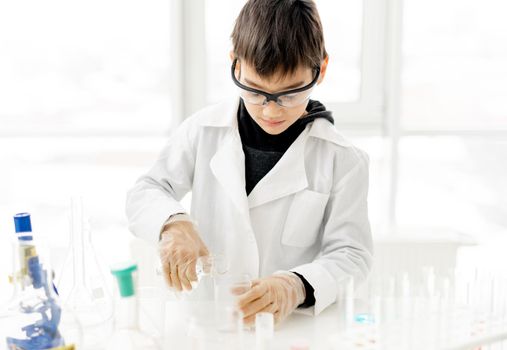 School boy wearing protection glasses doing chemistry experiment in elementary science class. Pupil with equipment tubes in lab