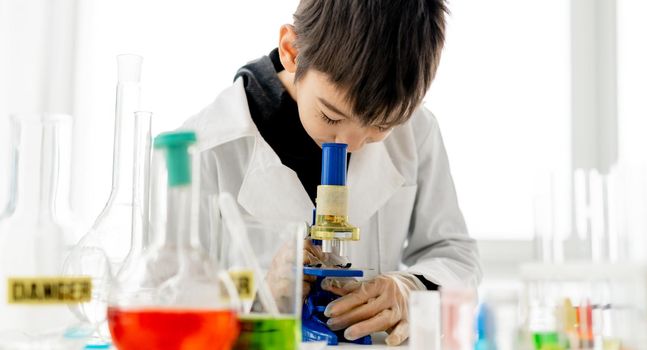 School boy doing chemistry experiment in elementary science class with microscope. Clever pupil with tubes in lab during test