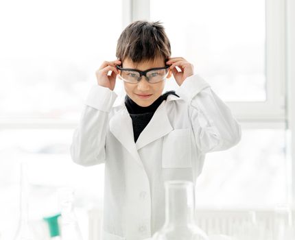 School boy wearing protection glasses doing chemistry experiment in elementary science class. Pupil with equipment in lesson