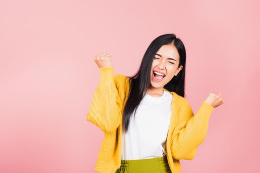Happy Asian portrait beautiful cute young woman standing winning and surprised excited screaming open mouth raise hands, studio shot isolated pink background, Thai female wow with copy space