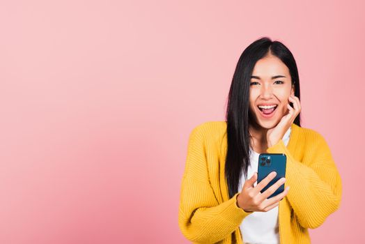 Happy Asian portrait beautiful cute young woman teen smiling excited using smart mobile phone studio shot isolated on pink background, Thai female surprised making winner gesture on smartphone