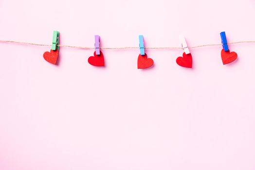 Happy Valentine's day concept. red heart-shaped valentines decoration hanging with wood clips for love on the rope isolated on pink background with copy space