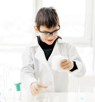 School boy wearing protection glasses doing chemistry experiment in elementary science class. Pupil with equipment tubes in lab during test