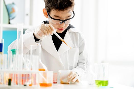 School boy wearing protection glasses with dirty face doing chemistry experiment with chemical liquids in elementary science class. Clever pupil analyzing results of test in lab