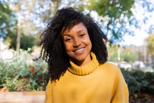 Portrait of smiling African American woman looking at camera wearing yellow sweater in a park. Lifestyle concept.