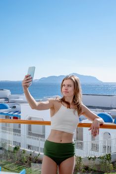 Vacation and travel. Happy woman in swimsuit taking selfie on mobile phone standing on the balcony of the hotel room, sea view