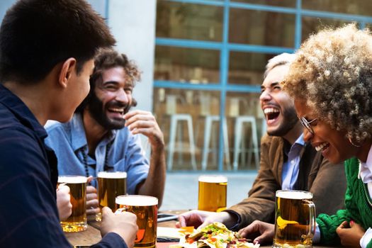 Laughing out loud. Multiracial friends enjoying beer together in a brewery bar. Friendship concept.
