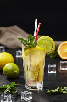 Fresh citrus lemonade with lemon, lime and orange served with ice and aromatic mint on black background. Refreshing summer drinks concept