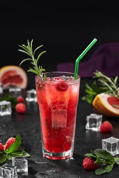 Refreshing raspberry and rhubarb lemonade with ice garnished with sprig of aromatic rosemary on black background. Healthy summer drinks concept