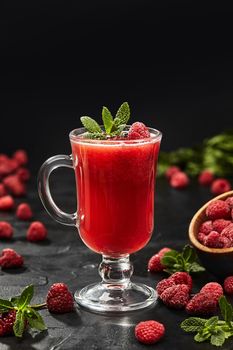 Refreshing cold berry tea from ripe raspberry served in glass with crushed ice garnished with fresh mint leaves on black background. Seasonal summer drinks concept