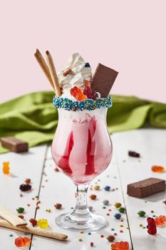 Fresh tasty berry milkshake topped with whipped cream, chocolate waffles, gummy bears and multicolored dragee in glass garnished with sprinkles. Sweet drinks for summer concept