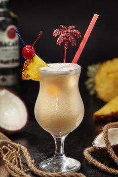 Classic white rum based Pina Colada cocktail with tropical flavours of pineapple and coconut traditionally garnished with pineapple wedge and maraschino cherry on black background