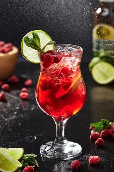 Refreshing berry and citrus low alcohol spritz cocktail from apple cider with Campari liqueur, ripe raspberries, lime and aromatic mint leaves on black background