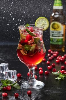 Refreshing low alcohol cocktail from apple cider with cranberries and aromatic mint served with crushed ice and lime slice. Glass of drink standing in fine water spray on black background