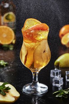 Sweetish light alcoholic cocktail with Aperol spritz, apple cider and pear syrup garnished with pears and orange slices served with ice on black background in fine water spray