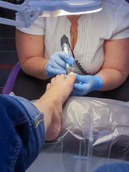 Master during a pedicure. The process of professional pedicures. The wizard in the mask causes the gel to the nails with a brush. The concept of beauty and health.