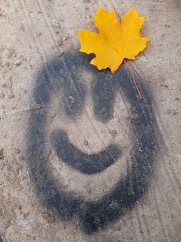 Smiley face on asphalt with yellow maple leaf.