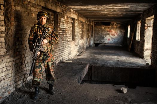 young soldiers with guns, A soldier in equipment and with arms inspects a ruined house outside the city.