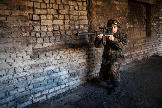 young soldiers with guns, A soldier in equipment and with arms inspects a ruined house outside the city.