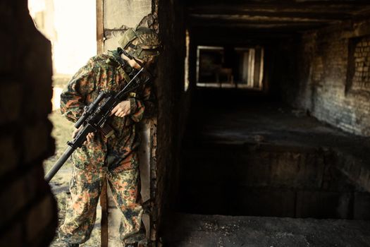 young soldiers with guns, A soldier in equipment and with arms inspects a ruined house outside the city.