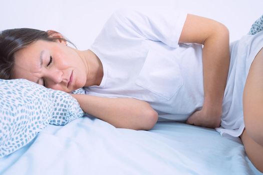 Young woman lying in the bed and suffering from gynecological problems, menstruation pain, stomach ache or abdominal pain. Menstruation period or PMS. High quality photo