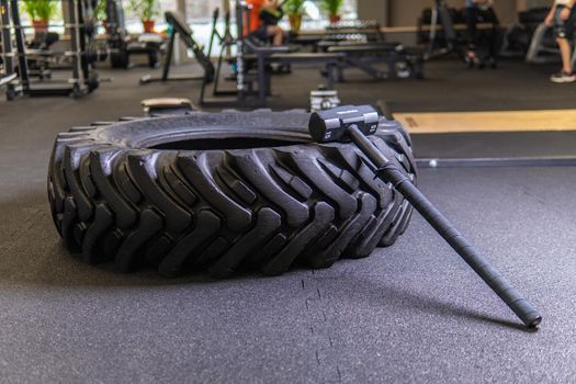 A tire on a black background with a sledgehammer lies for crosfit fitness wheel sledgehammer workout body tire, from fit exercise in bodybuilding health tyre, big build. Sweat indoors diet,