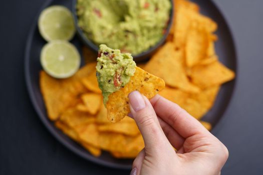 Closeup of woman hand with tortilla chips or nachos with fresh tasty guacamole dip. High quality photo