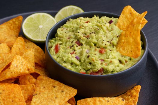 Guacamole dip with tortilla chips or nachos in black plate on a black background. High quality photo