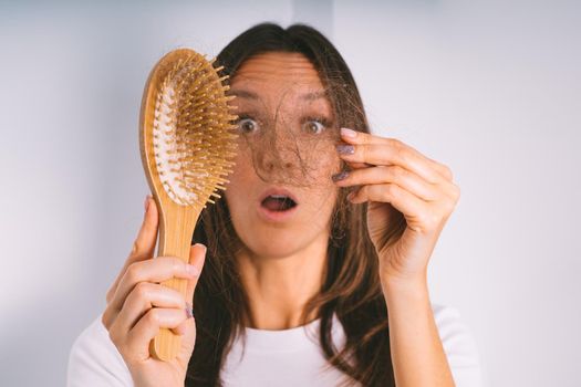 Young woman shocked because of hair loss problem. Woman holding hair brush and showing damaged hair. Bad hair falling out. High quality photo