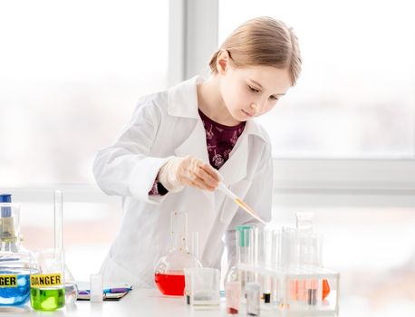 Smart girl during scientific chemistry experiment wearing protection glasses, holding tubes and measuring ingridients. Schoolgirl with chemical equipment on school lesson