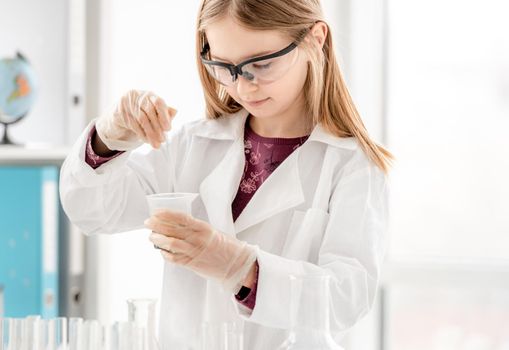 Girl doing scientific chemistry experiment wearing protection glasses. Schoolgirl with equipment and chemical liquids on school lesson